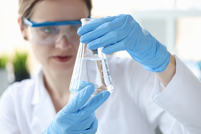 Mujer científica sosteniendo un frasco con líquido transparente en sus manos primer plano